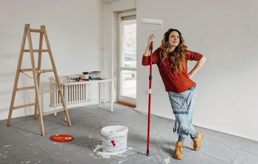 a woman holding a paint roller and a bucket of paint