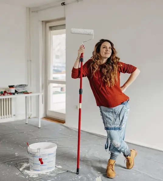 a woman holding a paint roller and a bucket of paint