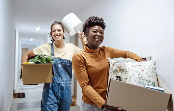 a couple of women carrying boxes and a plant