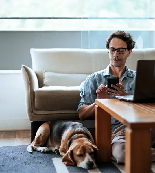 a man sitting on the floor with a dog and a laptop